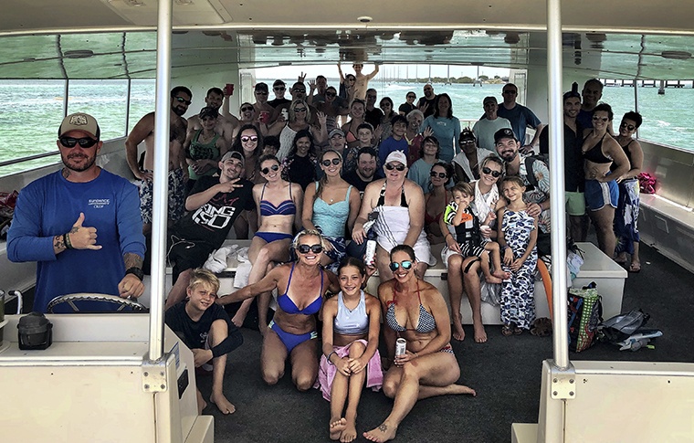 A large group of people all smiling for the camera in their swimming gear on board the boat